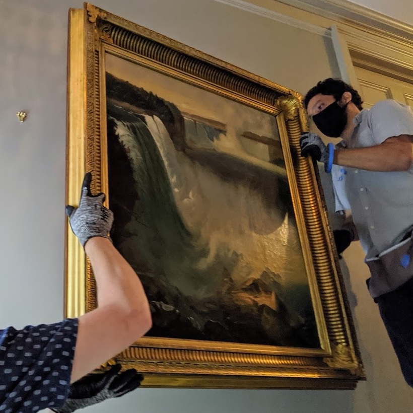 Art handlers moving large golden frame onto wall